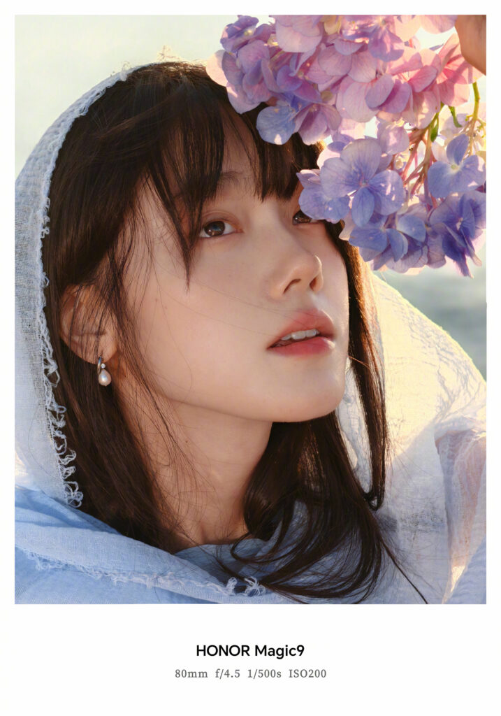 Photo d’exemple officielle du Honor Magic 9 prise de jour au téléobjectif de 80 mm : portrait d’une femme au foulard bleu, entourée d’hortensias