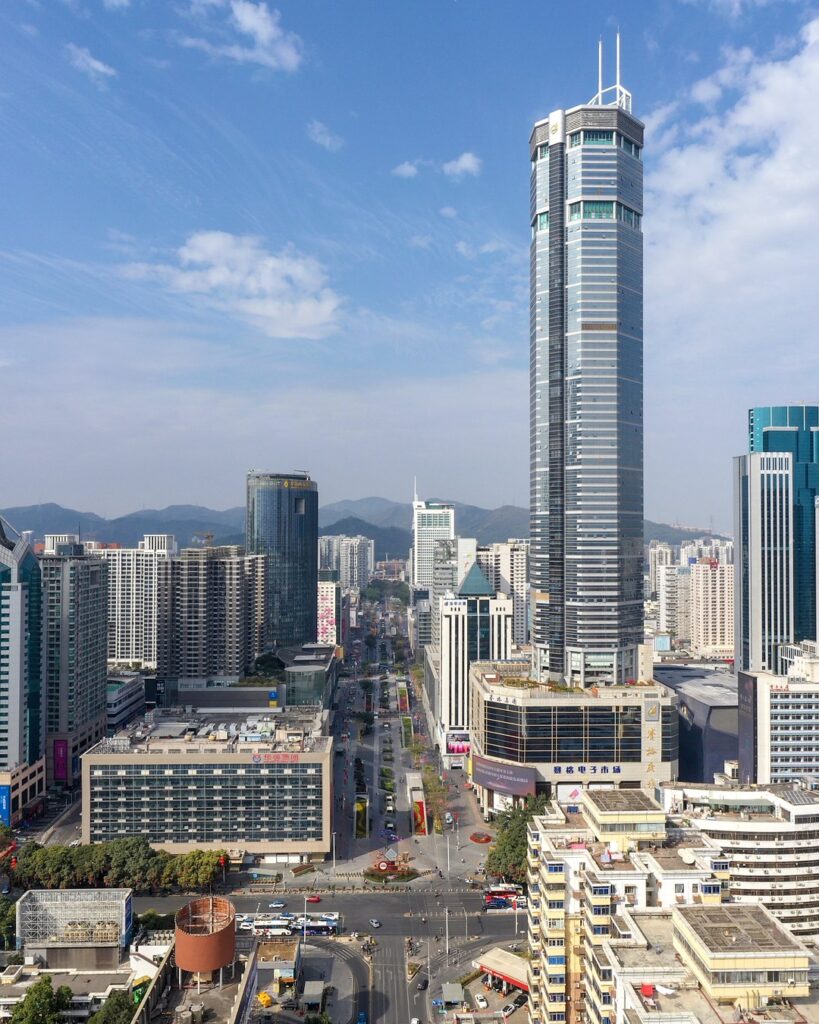 Vue aérienne du quartier de Huaqiangbei à Shenzhen : une longue avenue piétonne bordée d’immeubles, la tour SEG à droite et des montagnes à l’horizon